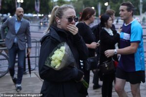 Une femme semble émue alors que les membres du public laissent des fleurs et des hommages devant le palais de Buckingham ce matin